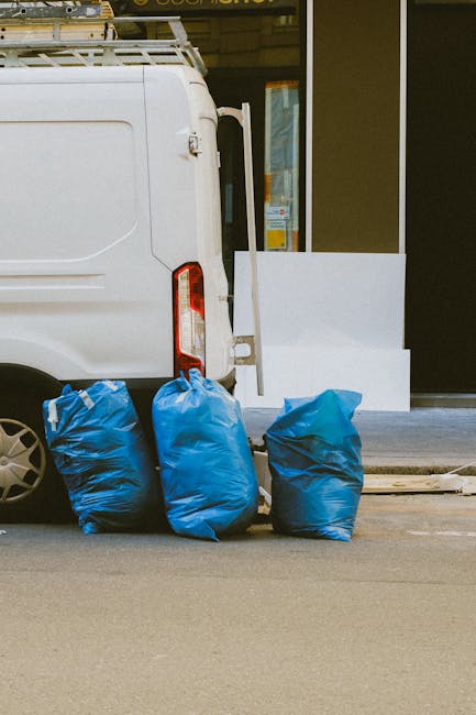 A human arm extending from the left side of the image holds a green plastic refuse bag filled with waste, with the bag's top gathered and tied in a knot. The bag is semi-transparent, showing the conte